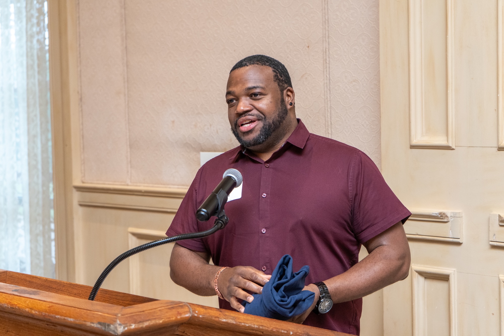 A Student speaks a lecturn while holding a crimson club t-shirt.