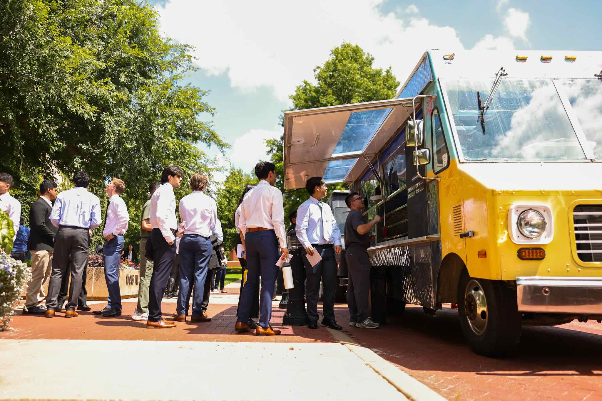 Students waiting in line in front of a yellow food truck.