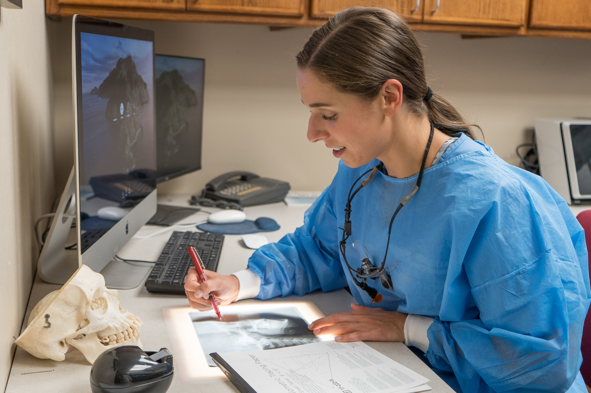 A student in a blue smock sitting at a desk reviewing an x-ray.