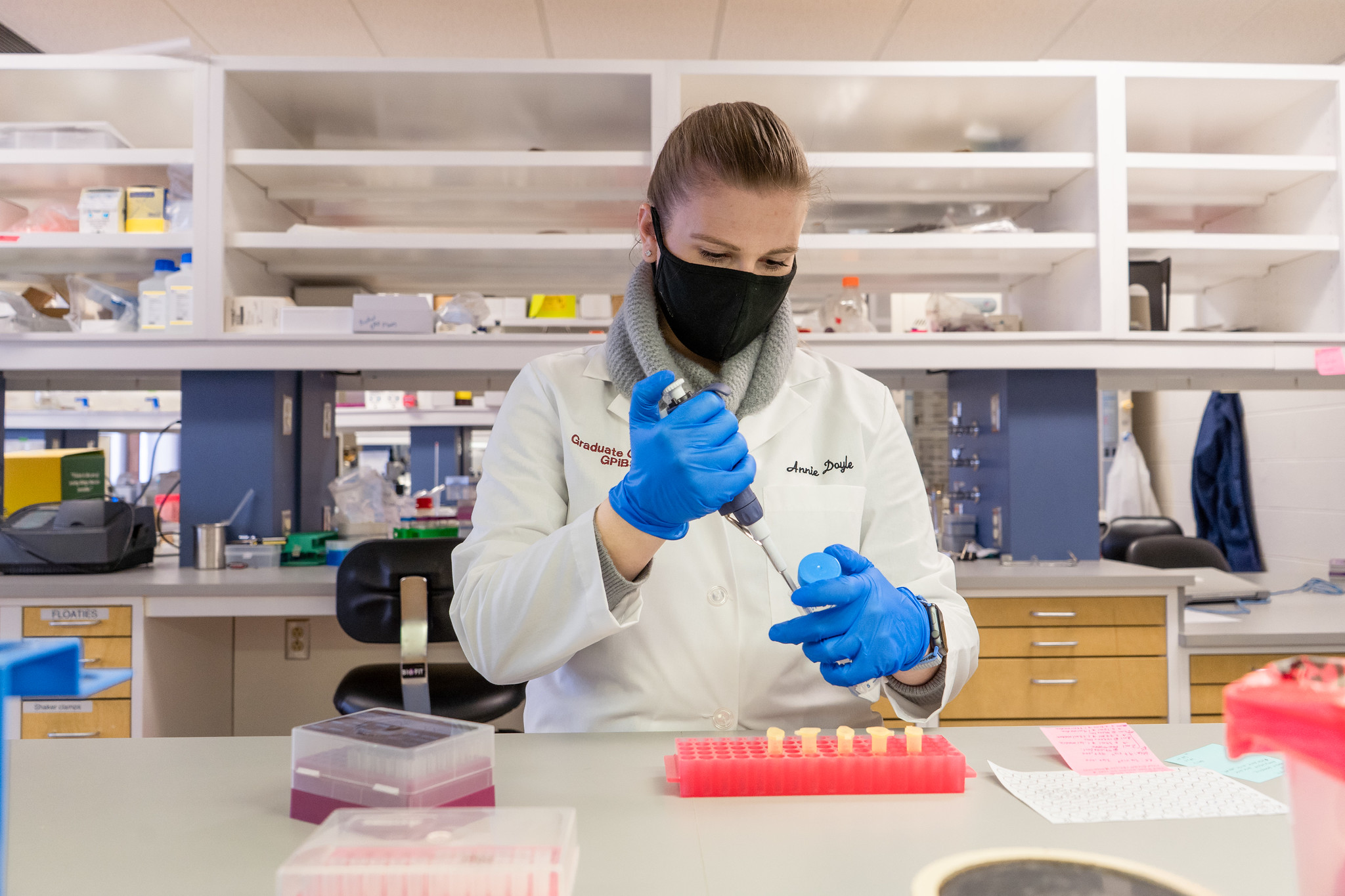 a student in a lab, wearing a white coat, extracting a substance from a vial using a needle