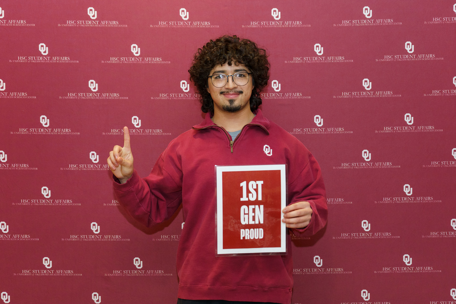 A first-generation student posing for a photo in front of a crimson backdrop.